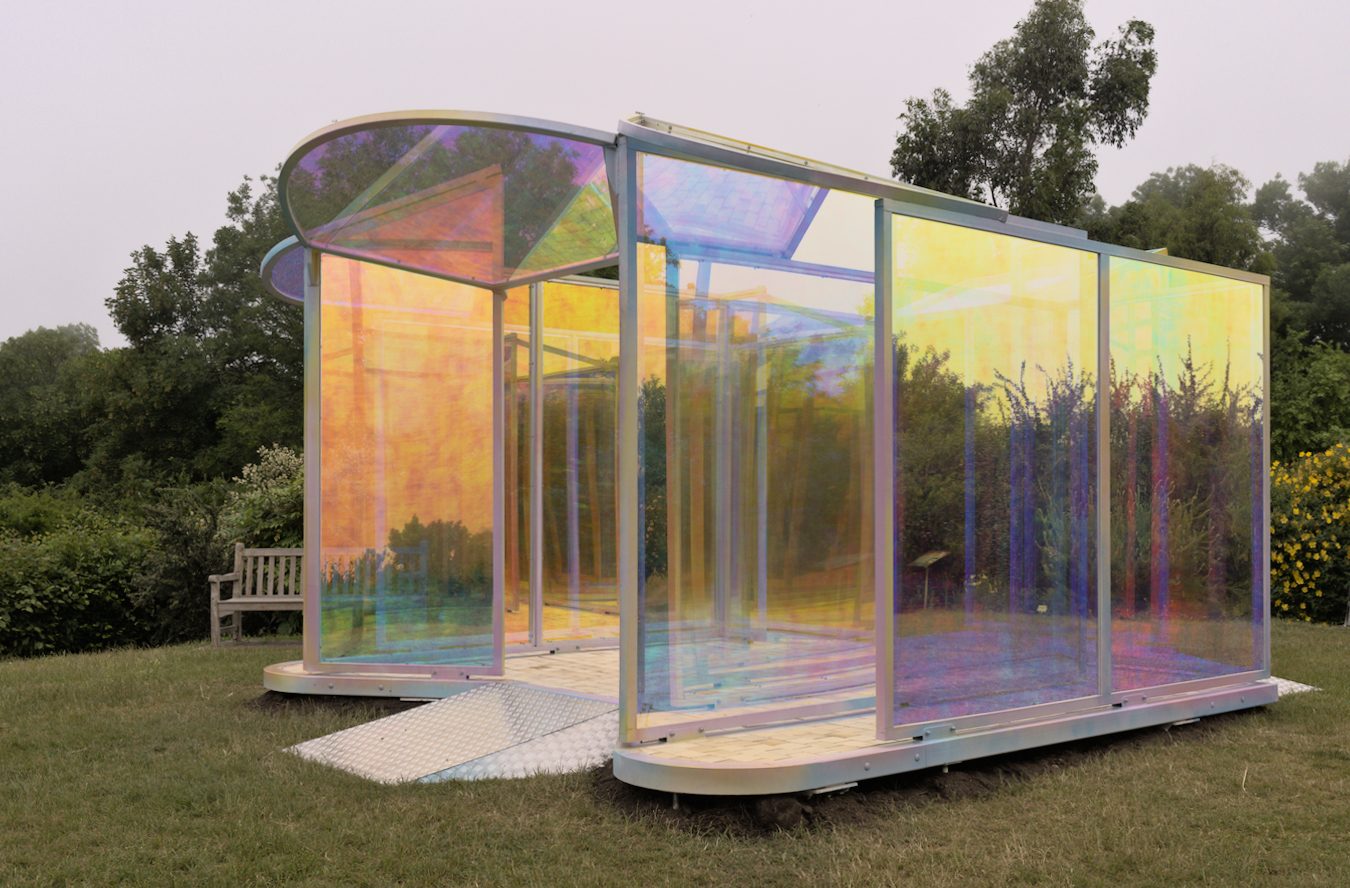 Pavillon de verre irisé sur une pelouse, toit courbe, végétation autour