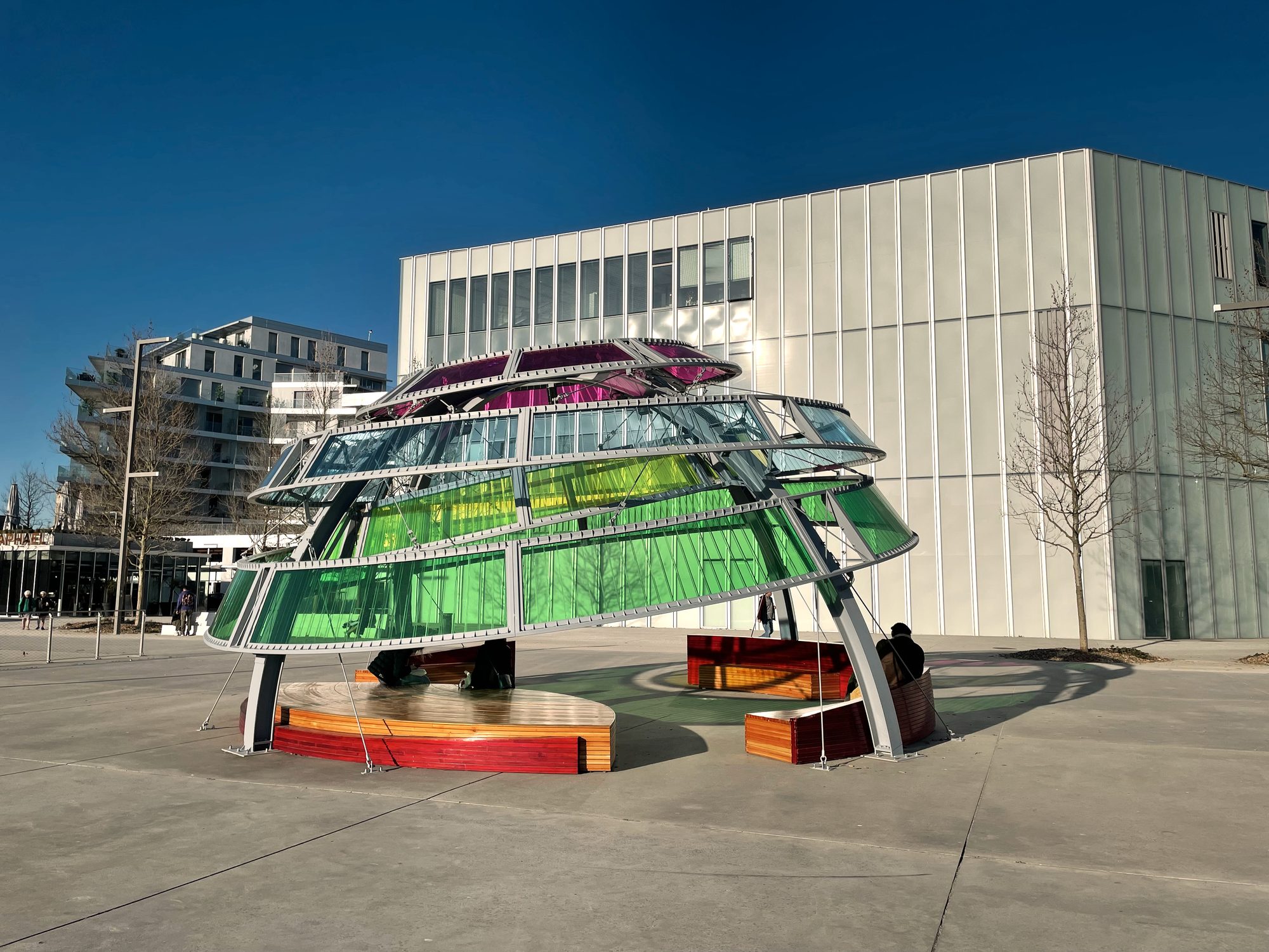 Coupole d’arcs métalliques et de panneaux translucides colorés devant un bâtiment blanc