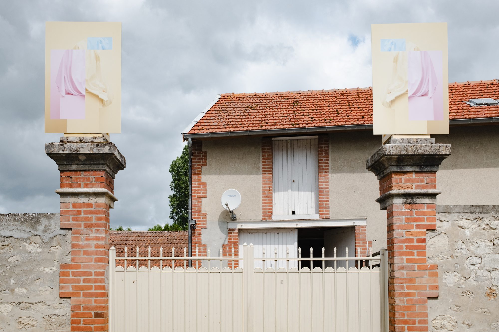 Deux photographies aux tons pastel posées sur les piliers de brique d’un portail