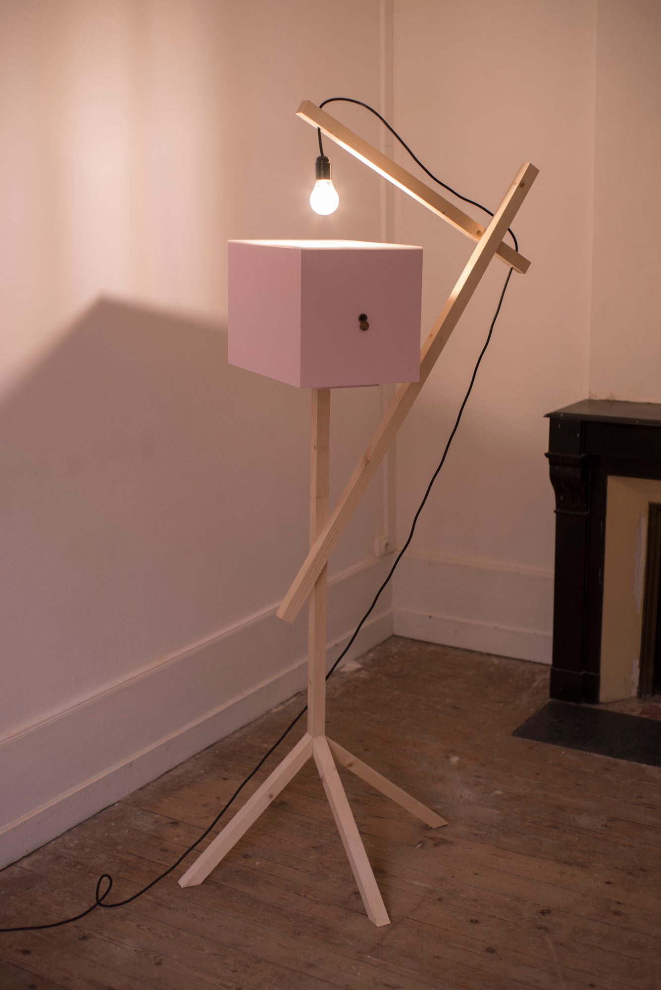 Boîte rose sur trépied en bois éclairée par une ampoule