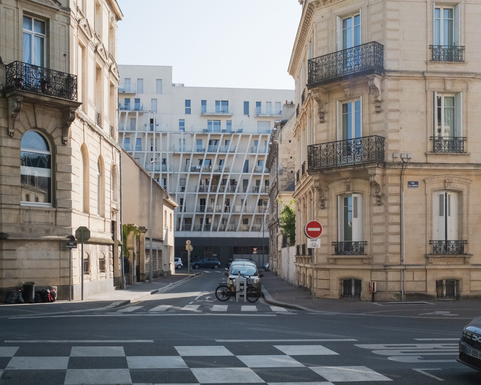 Carrefour entre deux immeubles anciens, façade moderne au fond