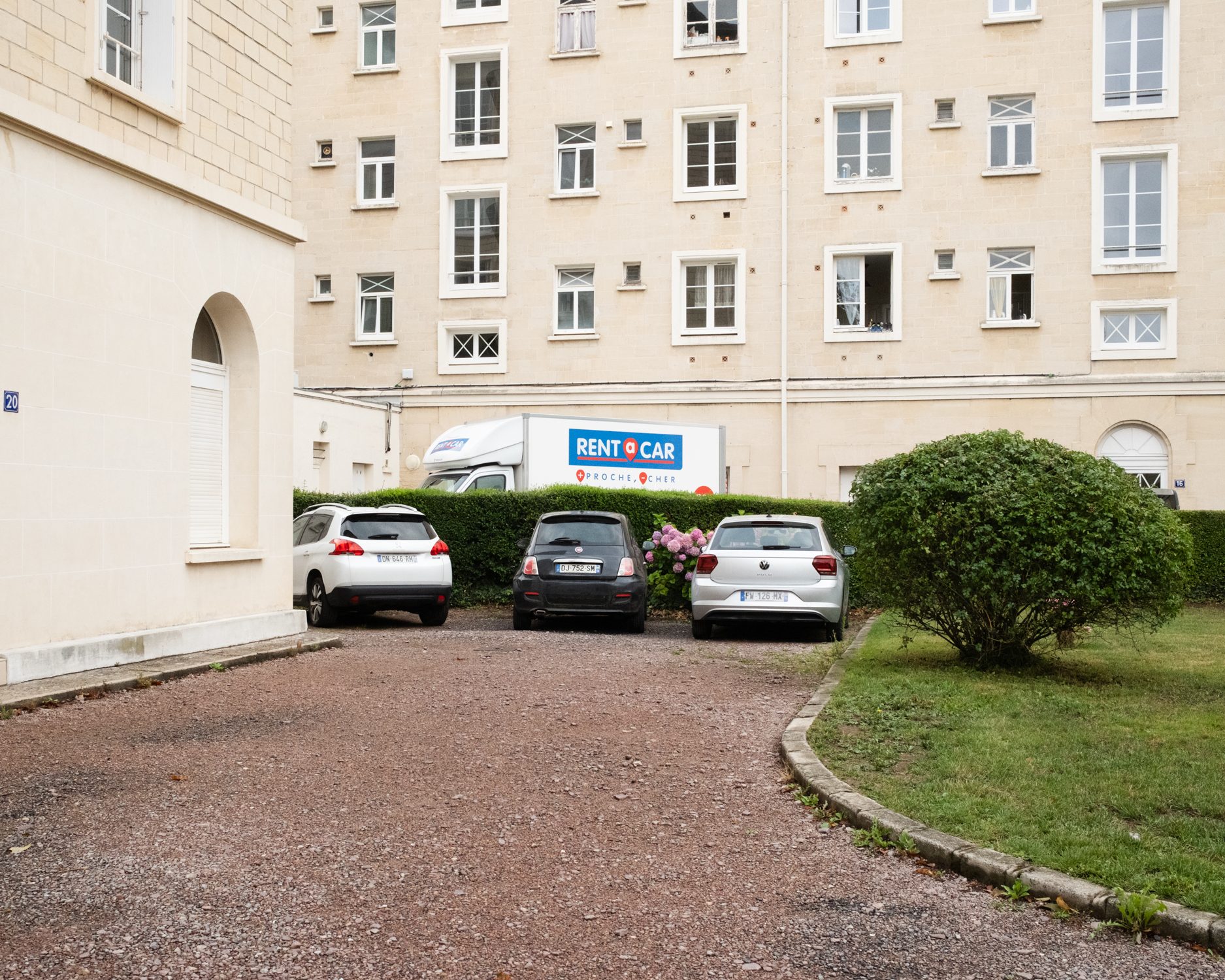 Cour d’immeuble avec voitures et buisson rond