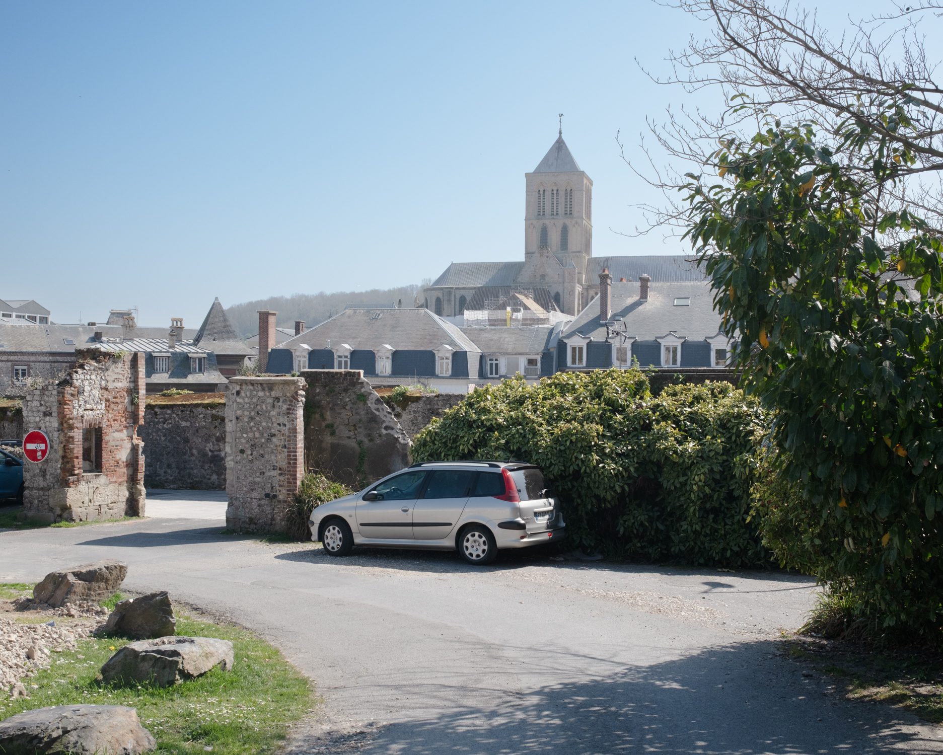 Parking devant un mur ancien, clocher au fond